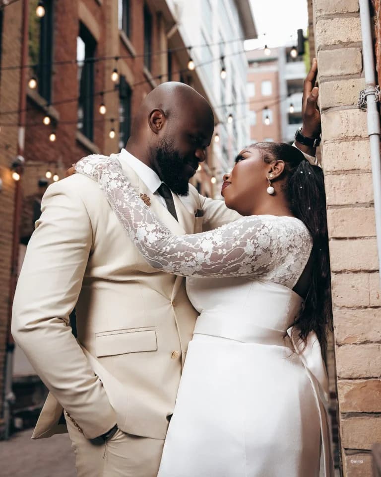 Couple in ivory attire embracing under string lights in brick alley