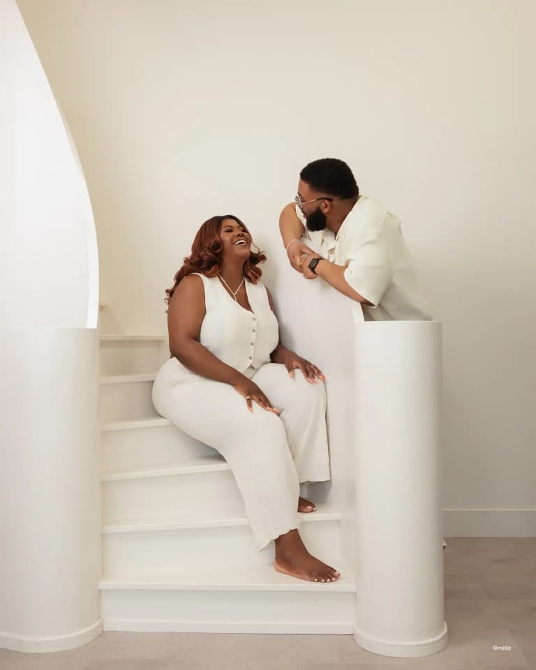 Couple in matching cream outfits sharing a laugh on a white spiral staircase