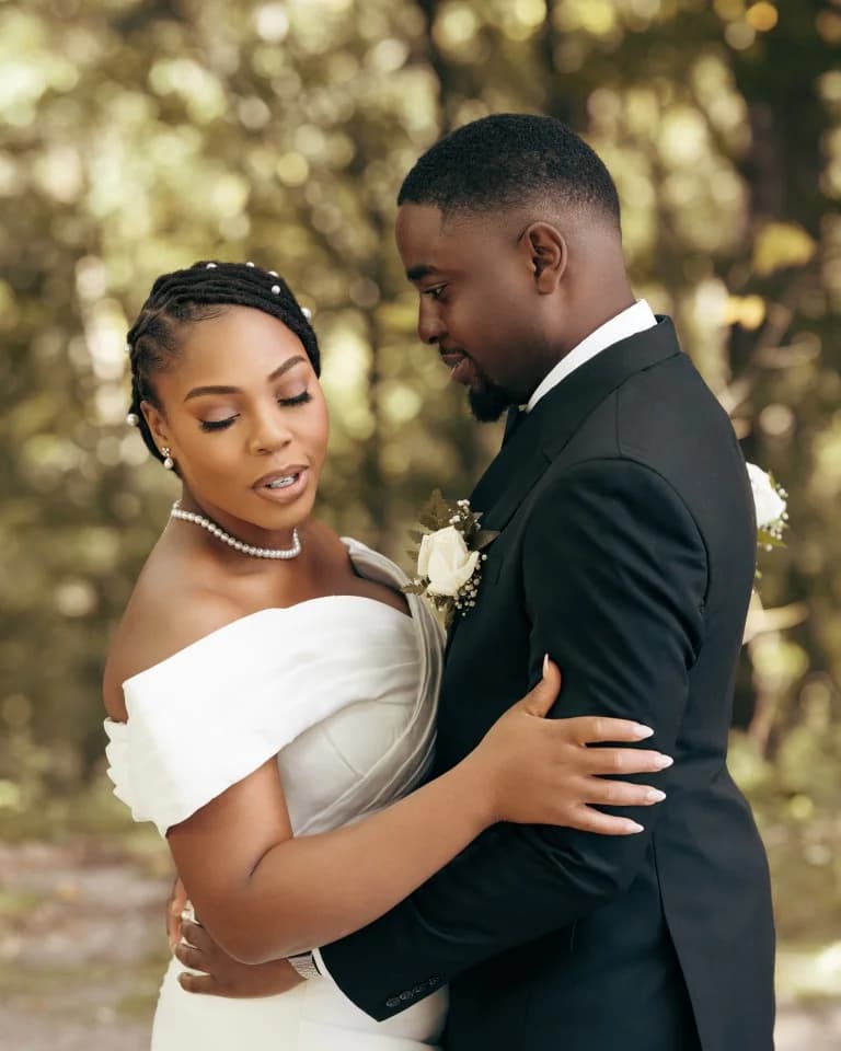 Bride with pearl-adorned braids embracing groom in black suit with white rose boutonniere