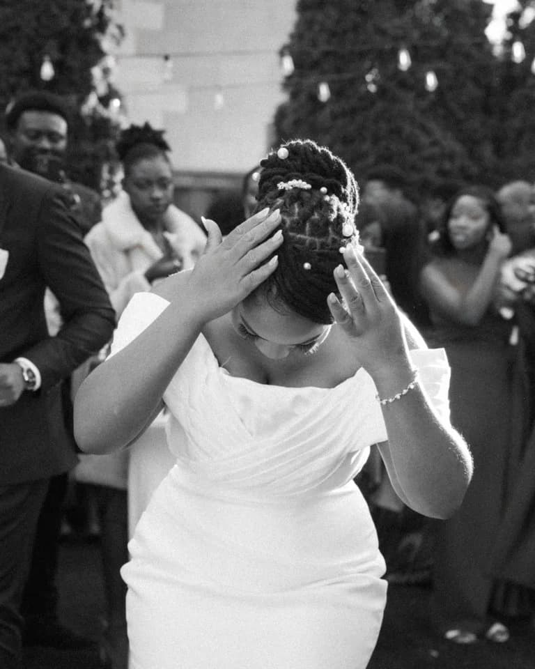 Bride bowing her head with hands raised to her pearl-pinned hair among guests