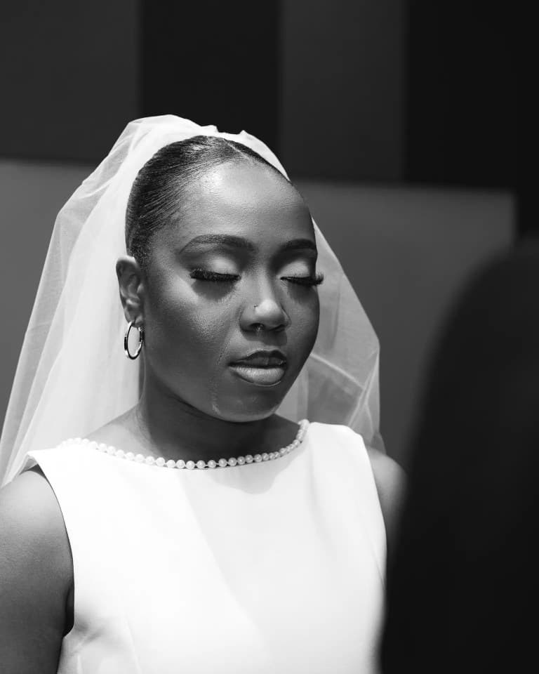 Bride with eyes closed wearing a veil, hoop earrings, and pearl-trimmed neckline