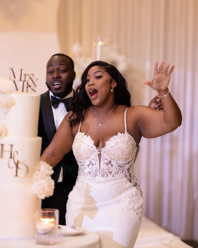 Excited bride and groom reacting beside tiered wedding cake with monogram toppers