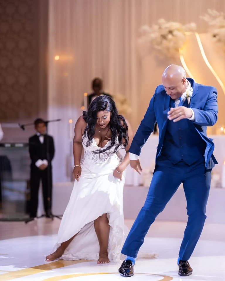 Bride and groom in blue three-piece suit dancing on a white ballroom floor