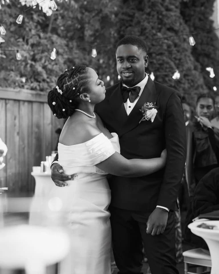 Bride gazing at groom in tuxedo as they embrace beneath string lights
