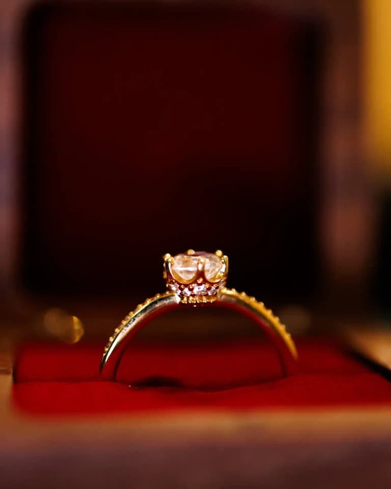 Gold solitaire engagement ring standing upright on red velvet ring box