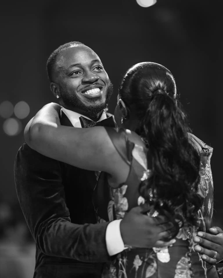 Smiling groom in velvet tuxedo embracing a woman in a floral gown while dancing