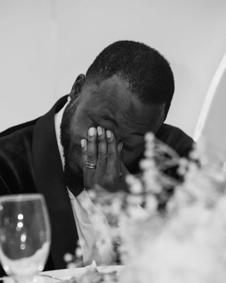Groom in velvet tuxedo covering his face with his hand at a reception table