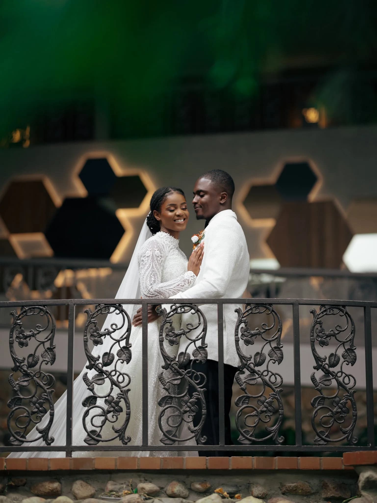 Bride in beaded gown embracing groom in white jacket behind ornate iron railing