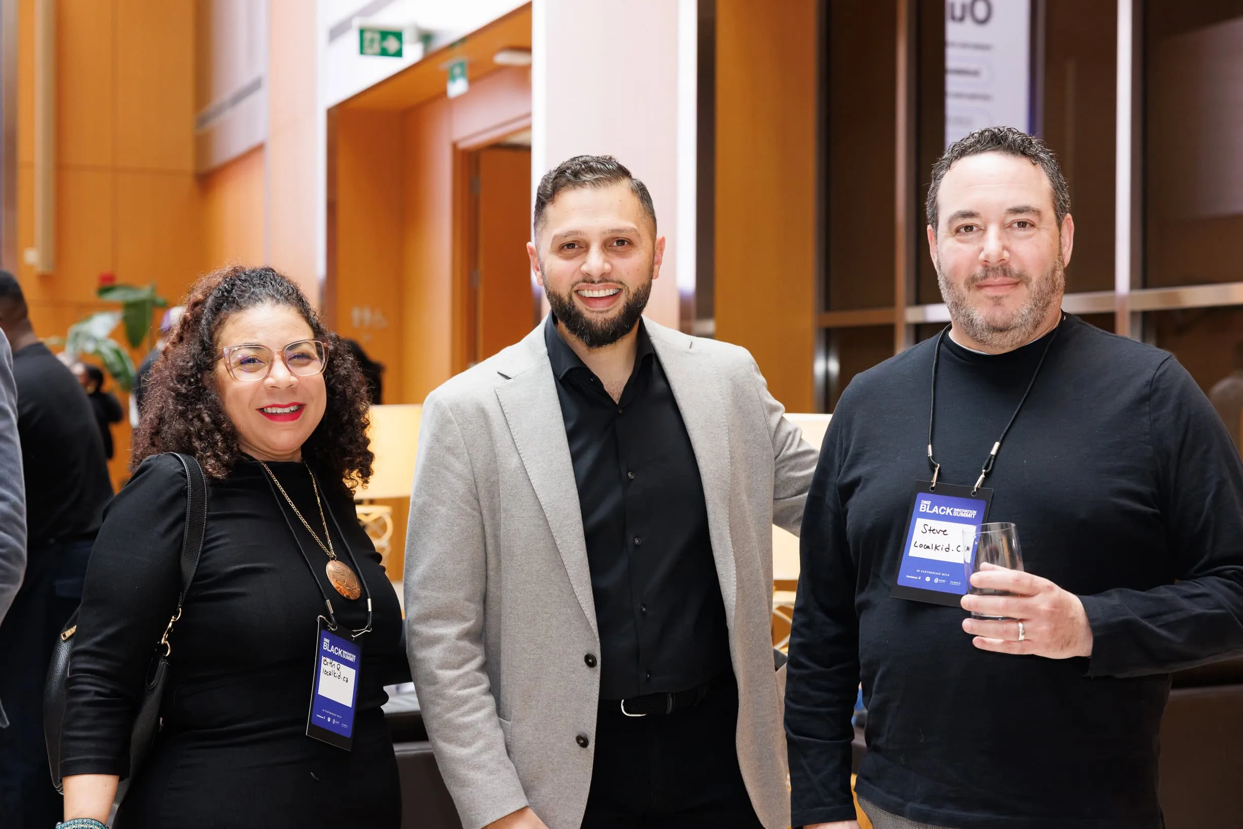 Three smiling professionals posing together wearing event lanyards at an indoor conference space