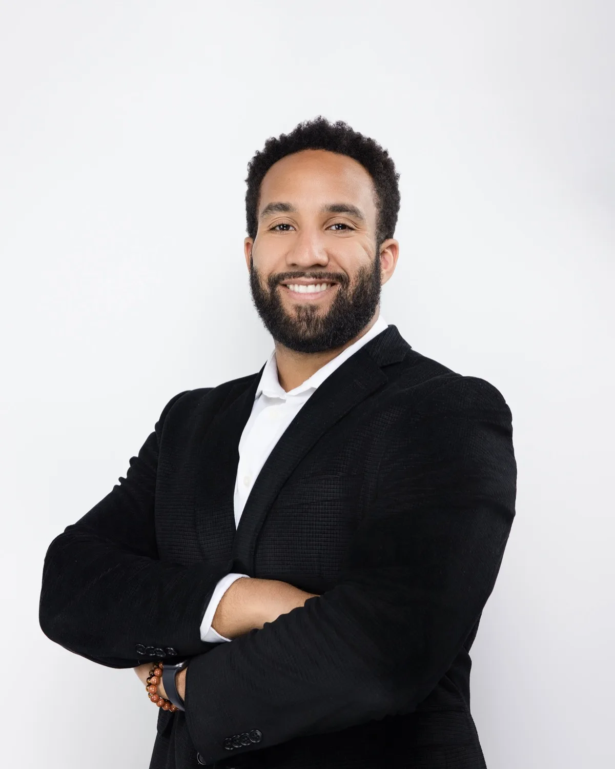 Smiling man with beard in black blazer and white shirt, arms crossed against white backdrop