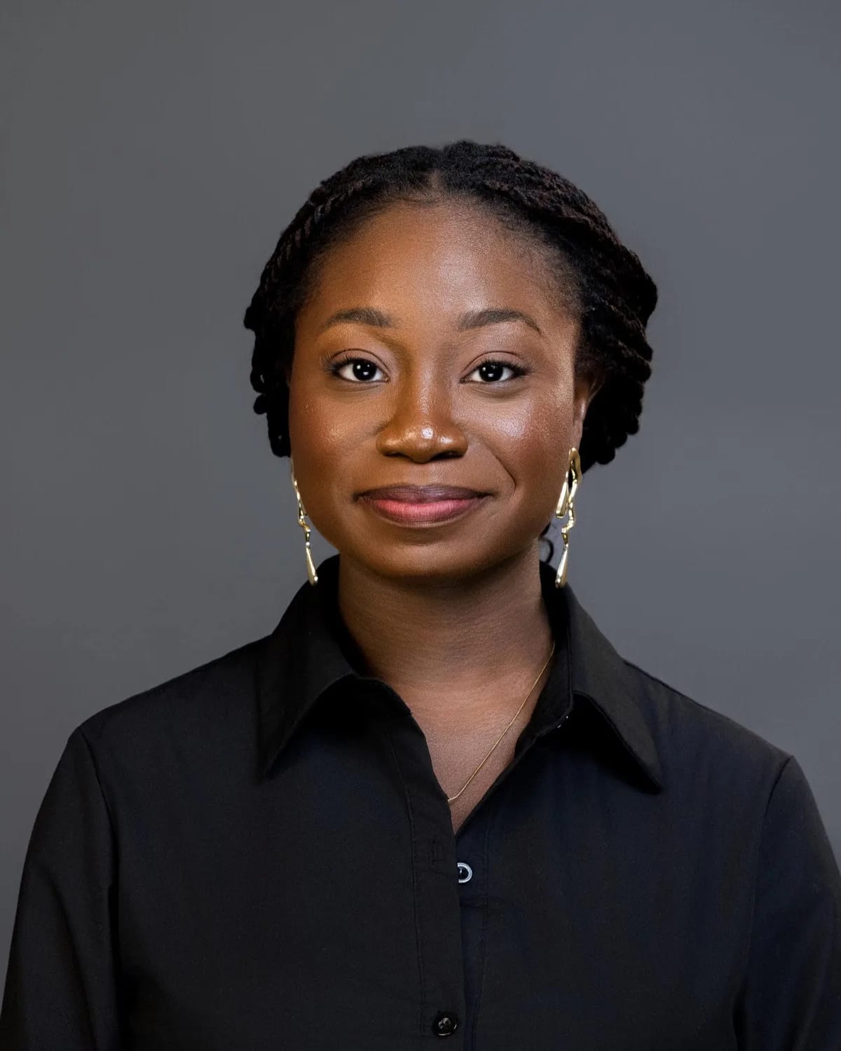 Woman with twisted hair and gold earrings in black button shirt against gray studio backdrop