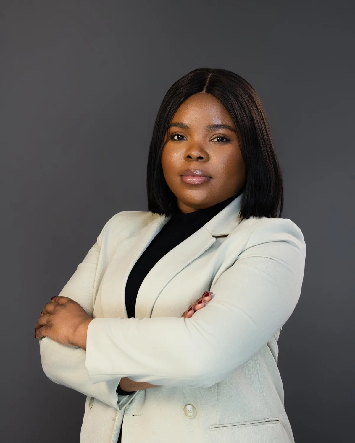 Woman with straight hair in pale mint blazer and black top, arms crossed against gray backdrop