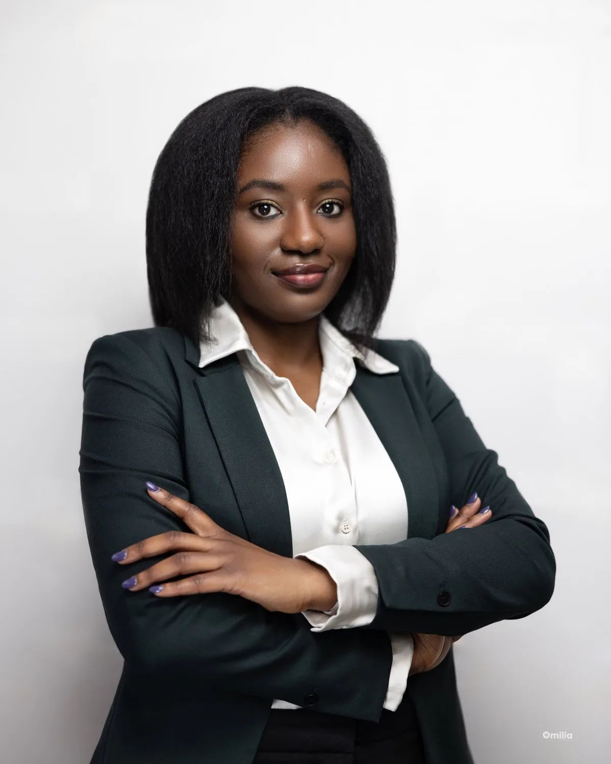 Woman with dark hair in navy blazer and white blouse, arms crossed against light backdrop