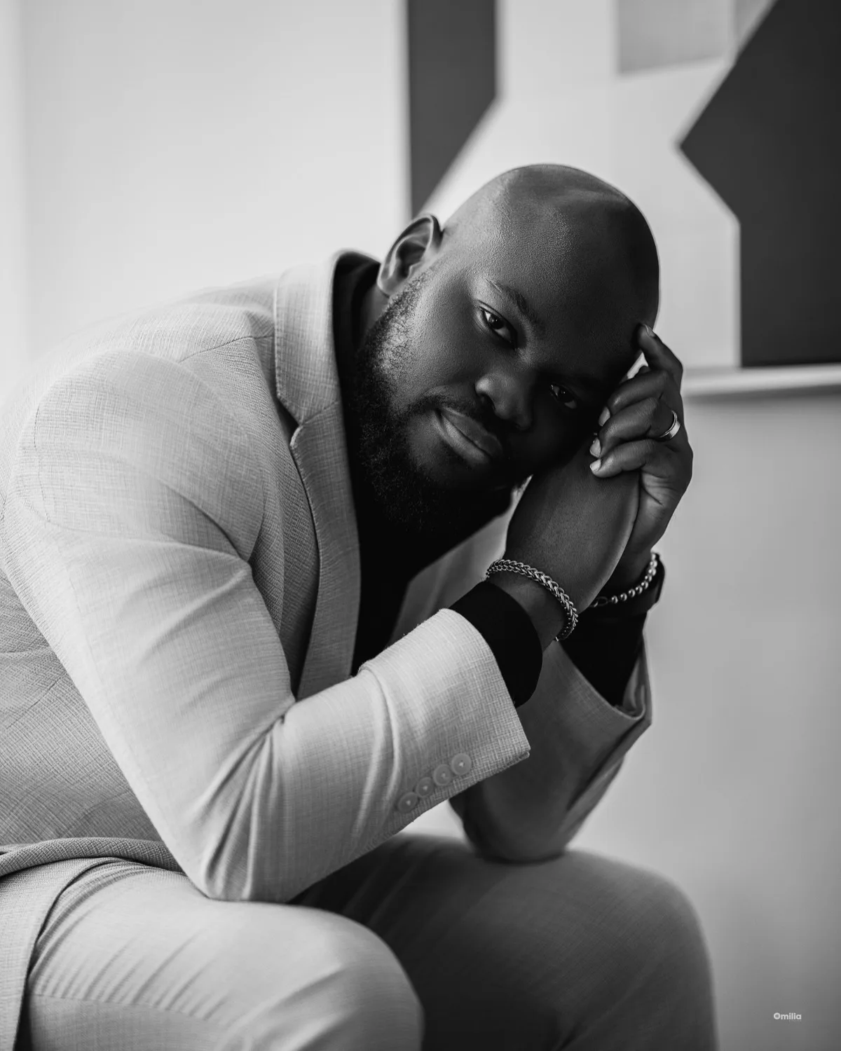 Black and white portrait of bald bearded man in light suit resting head on hand
