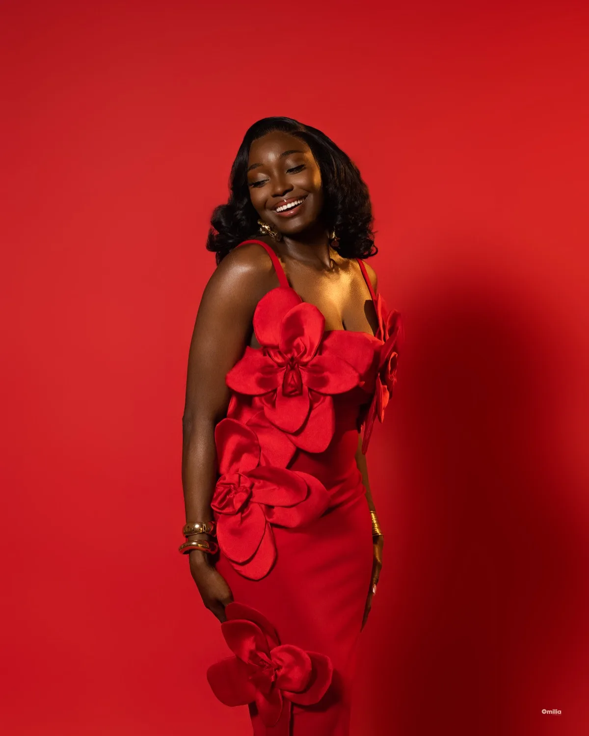 Smiling woman in red gown with three-dimensional floral appliqué against bold red backdrop