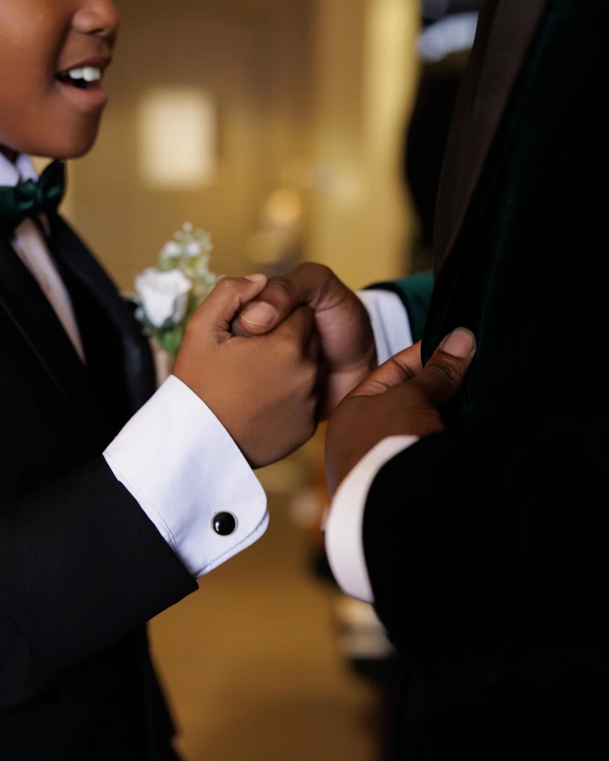 Young boy in tuxedo and green bow tie gripping a suited man's hand indoors