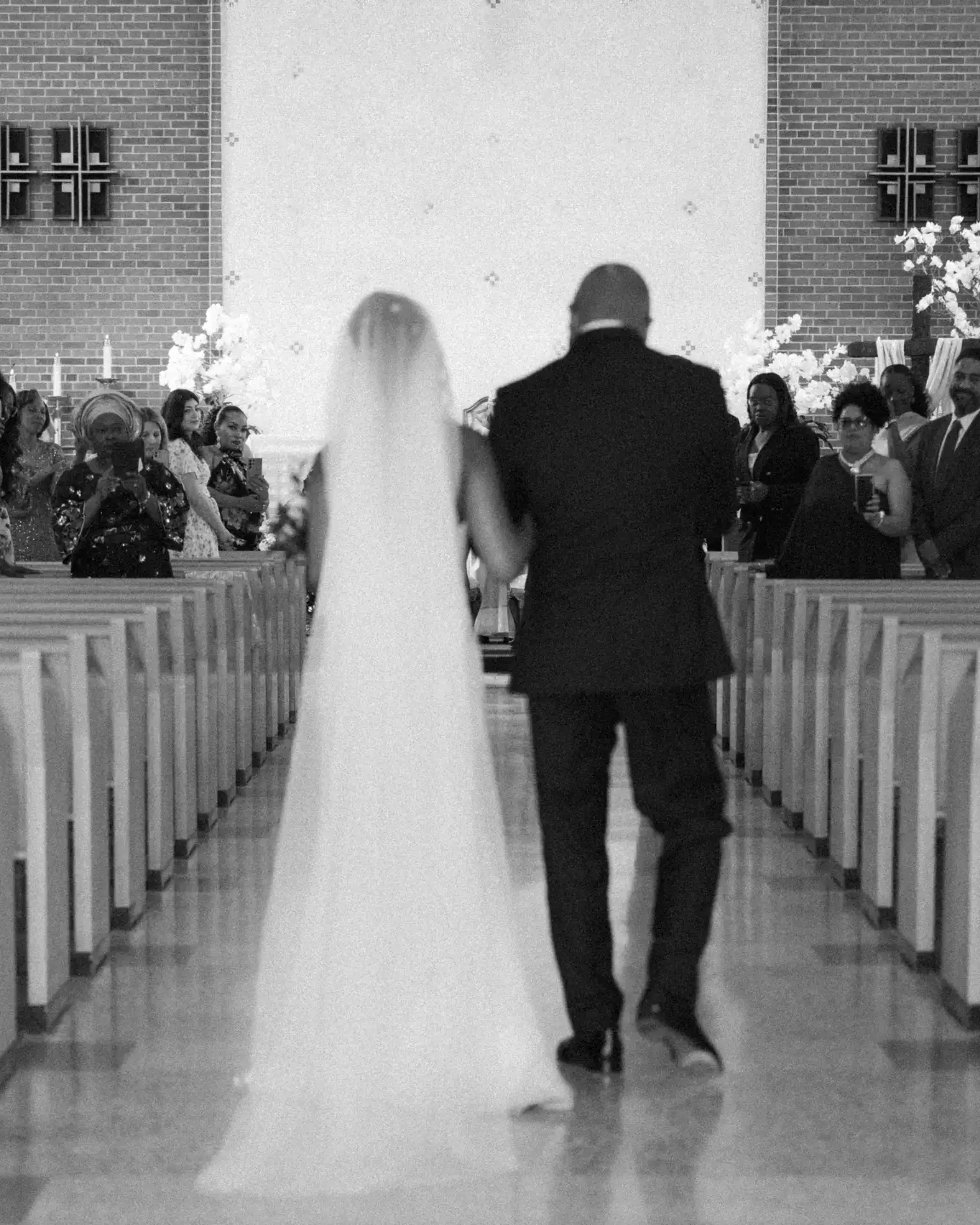 Bride with long veil escorted down the church aisle past standing guests
