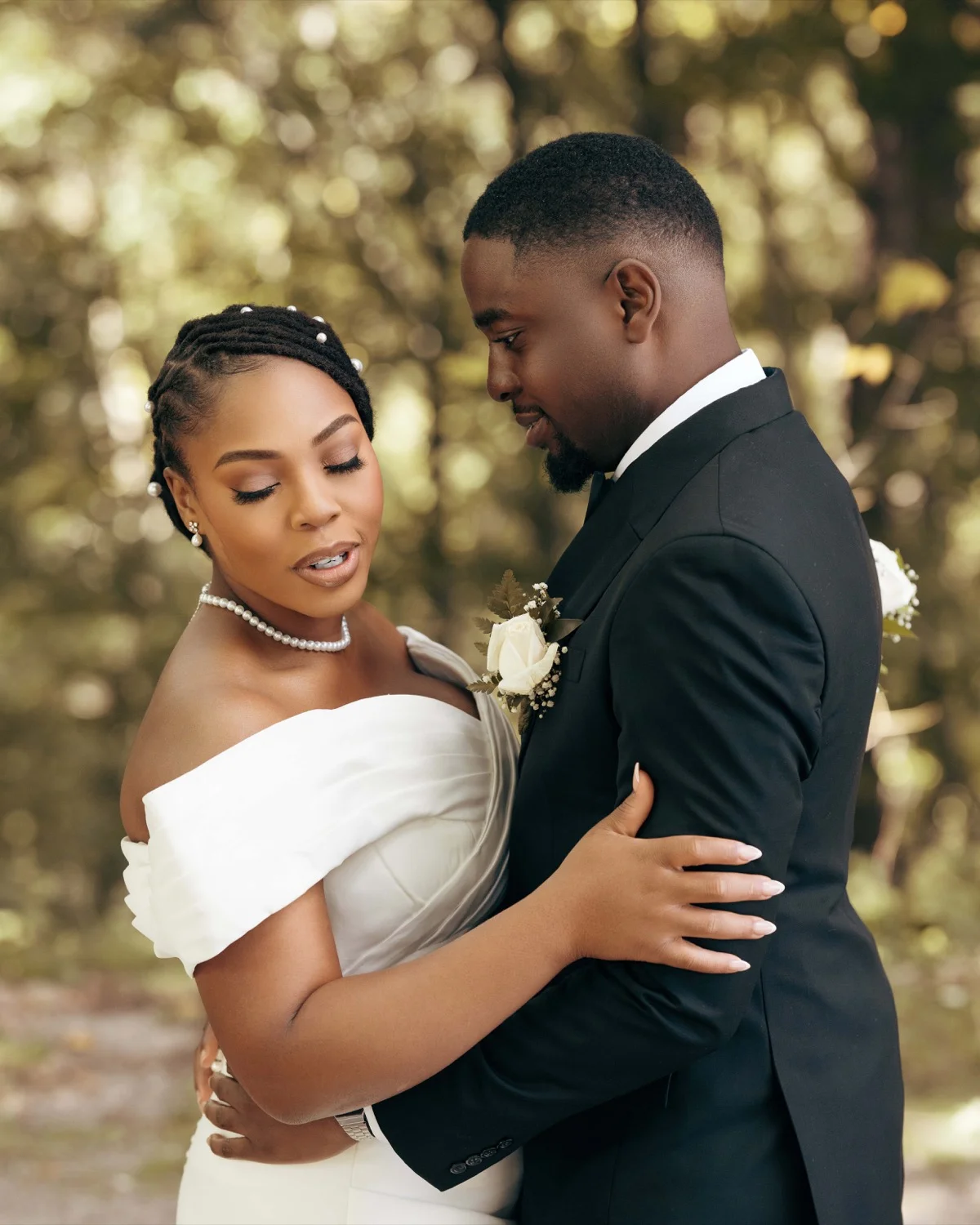Bride and groom in close embrace, pearl necklace and white rose boutonniere visible