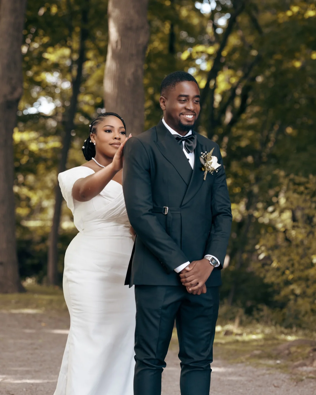 Bride reaching for smiling groom's shoulder during a first look on a wooded path