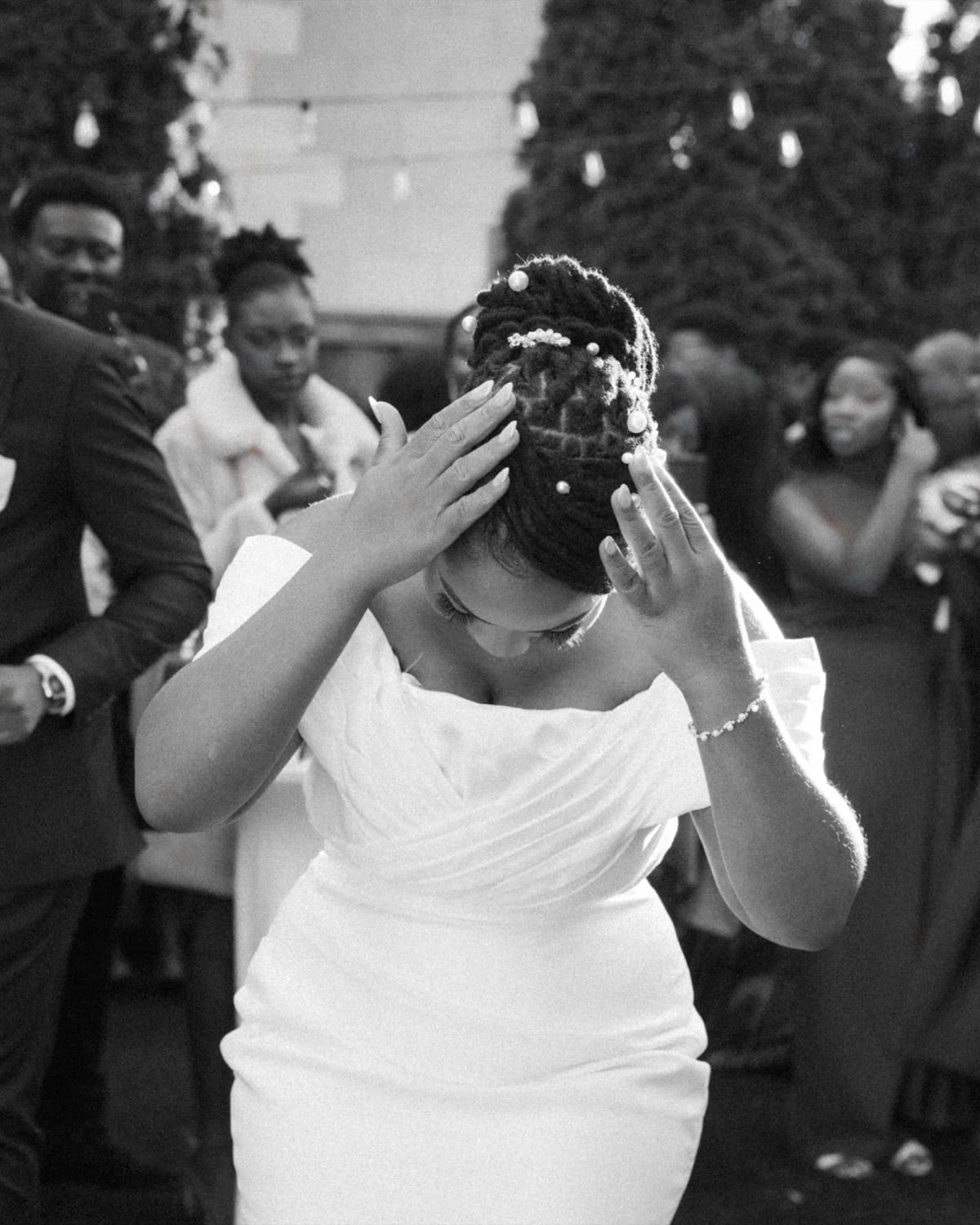 Bride raising hands to her pearl-studded updo while dancing among outdoor guests