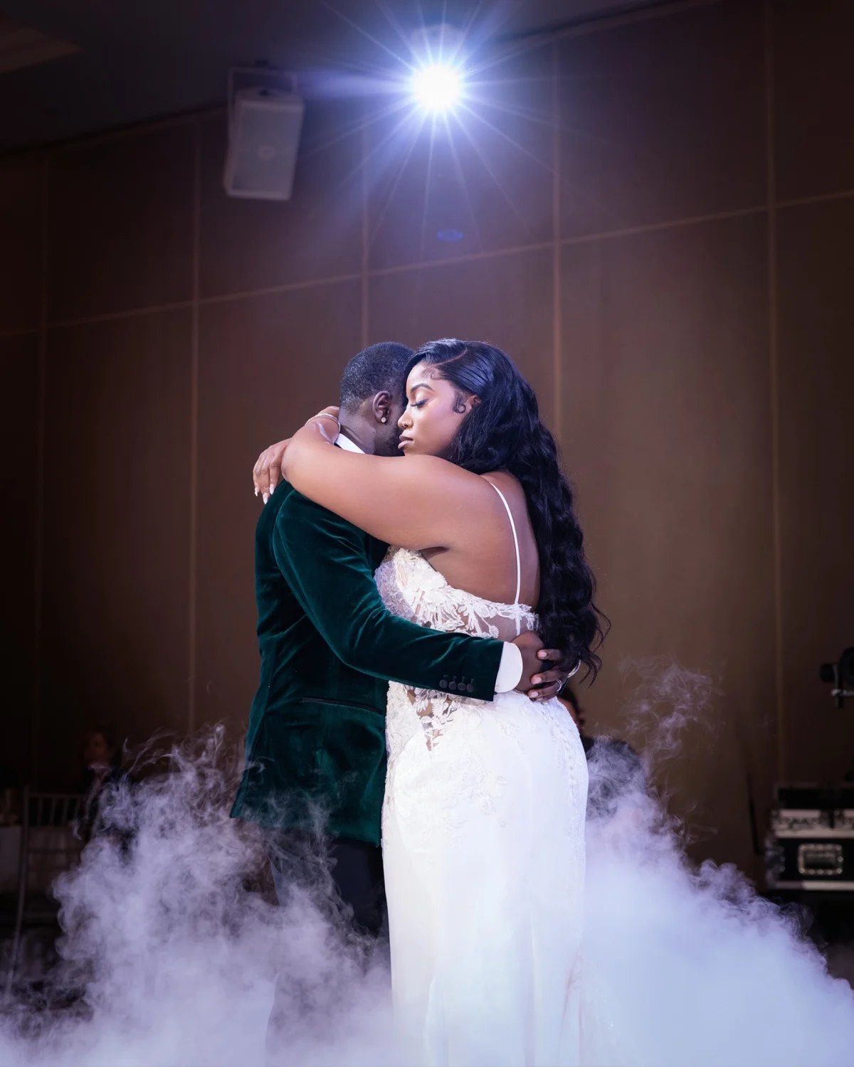 Bride and groom in green velvet jacket embracing during their first dance amid low fog