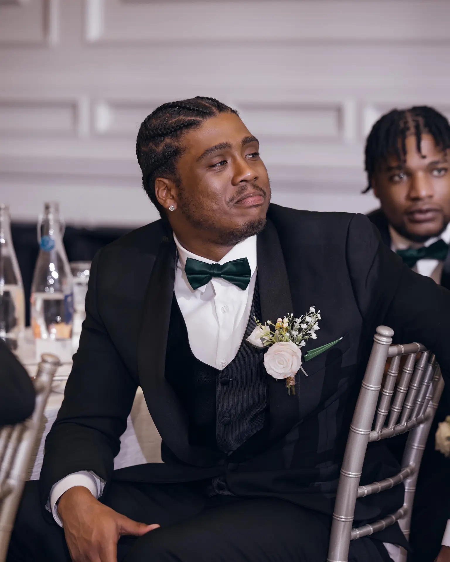 Man in black tuxedo with emerald bow tie and rose boutonniere seated at a reception table