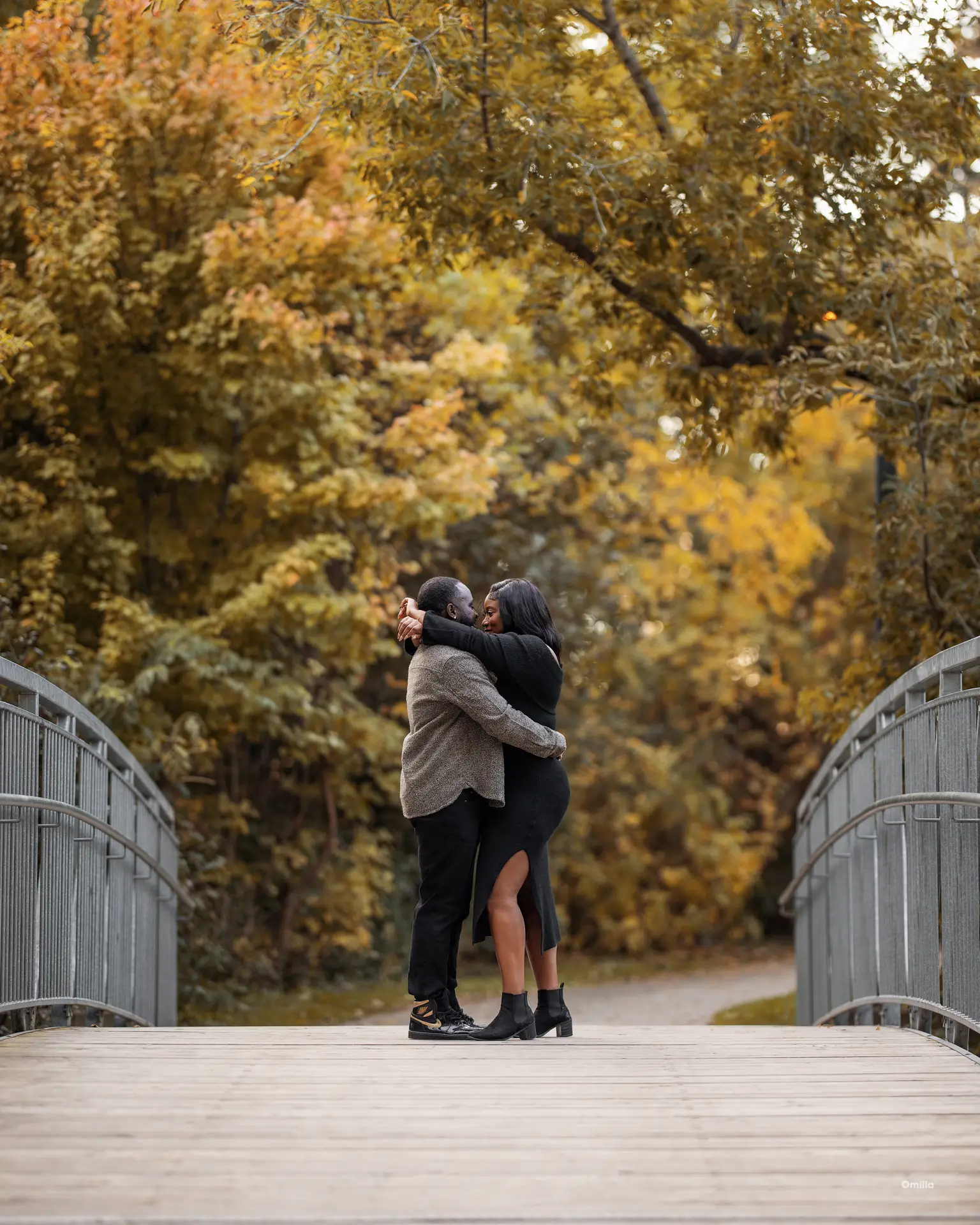 Couple embracing face to face on a footbridge framed by golden autumn foliage