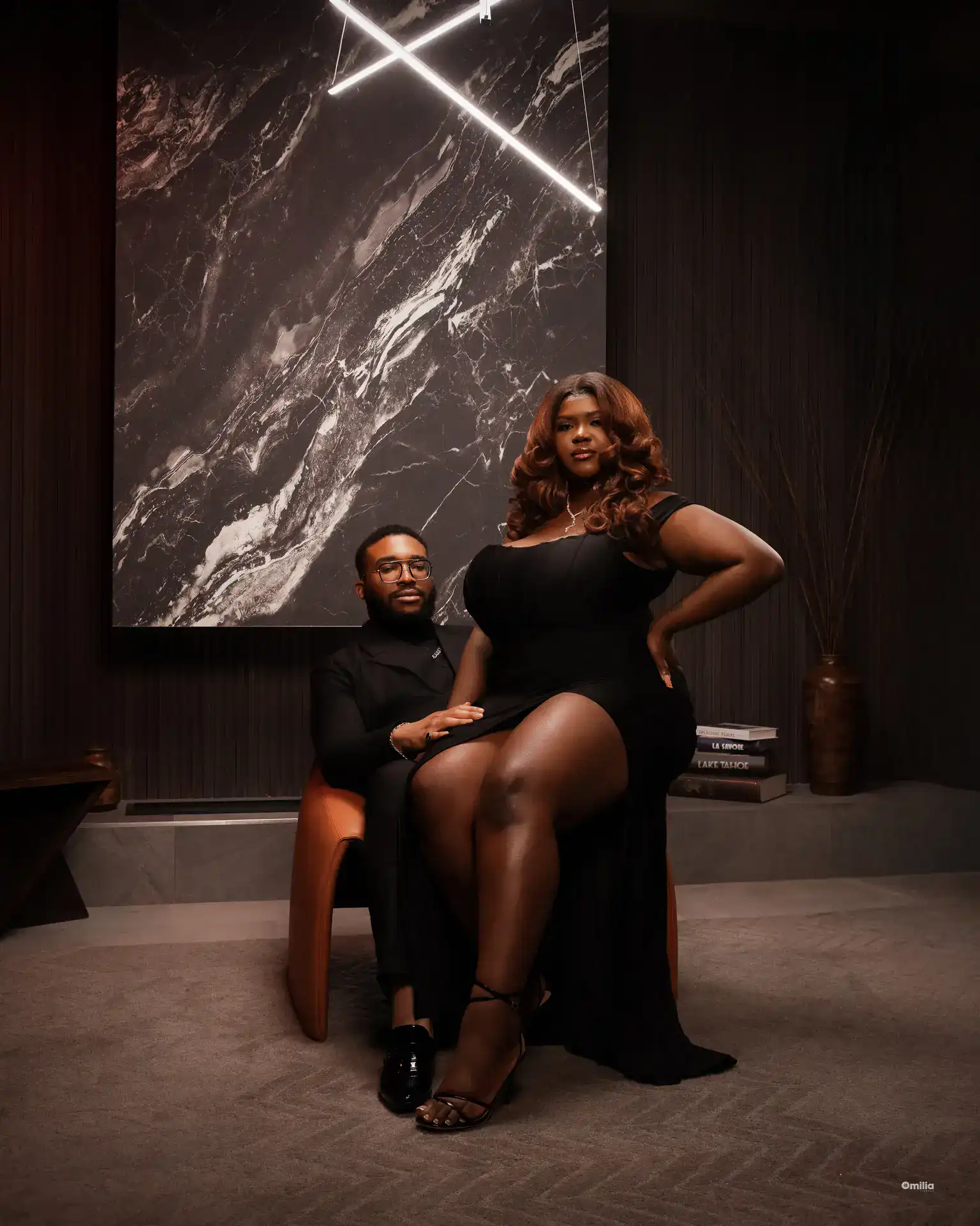 Couple in a dark lounge, woman in black slit dress seated on partner's lap
