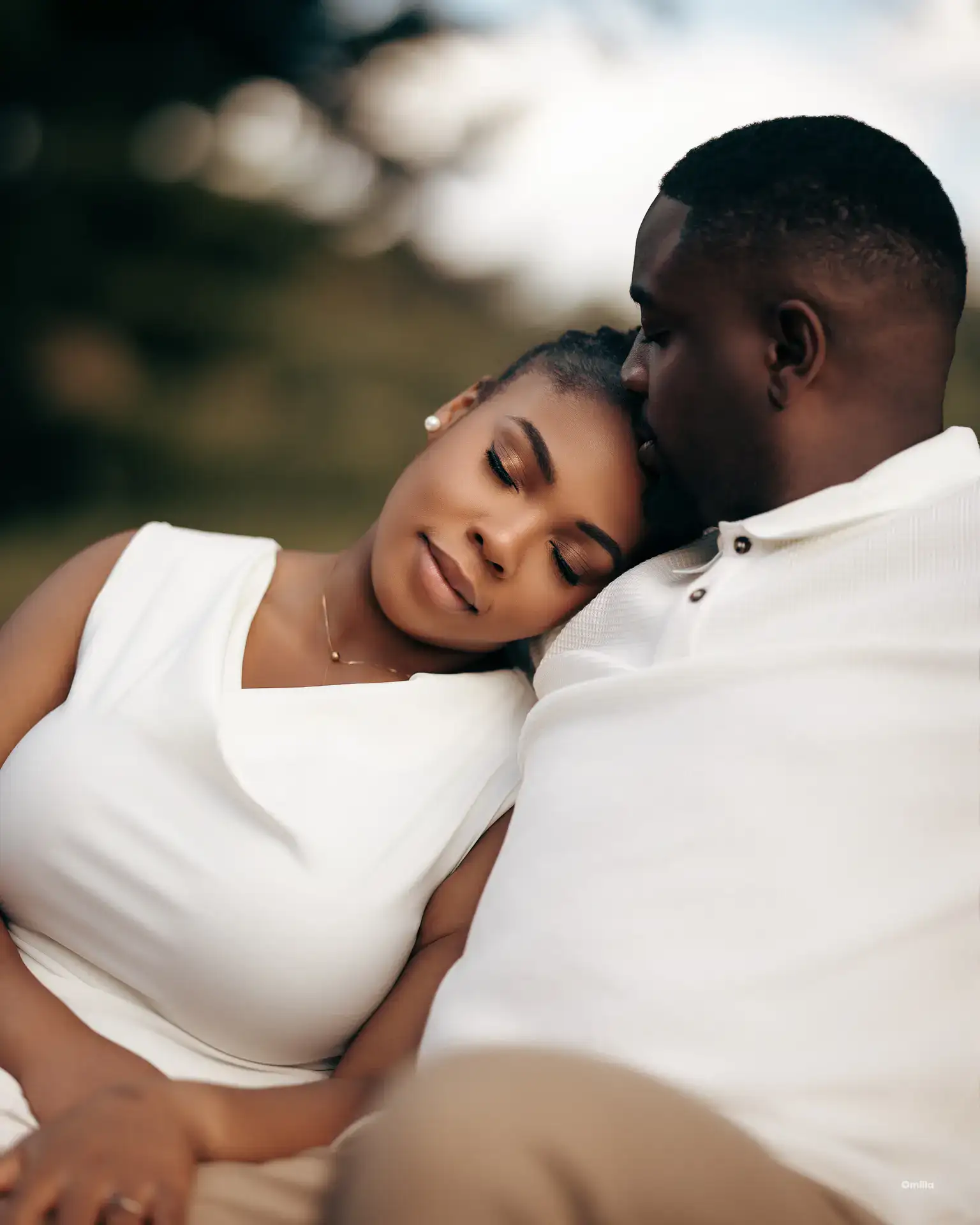 Woman in white dress resting her head on partner's shoulder outdoors at golden hour
