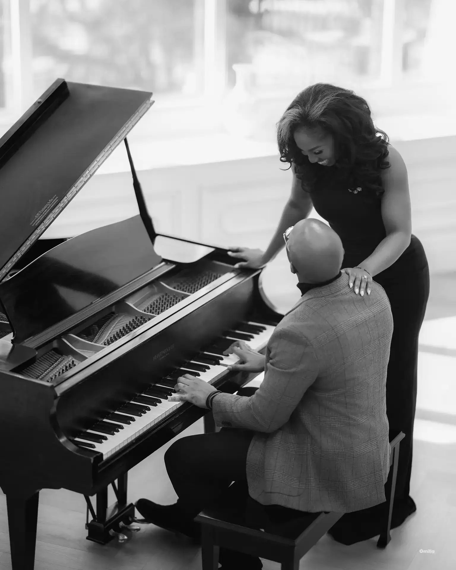 Man playing a grand piano while woman leans over his shoulder smiling