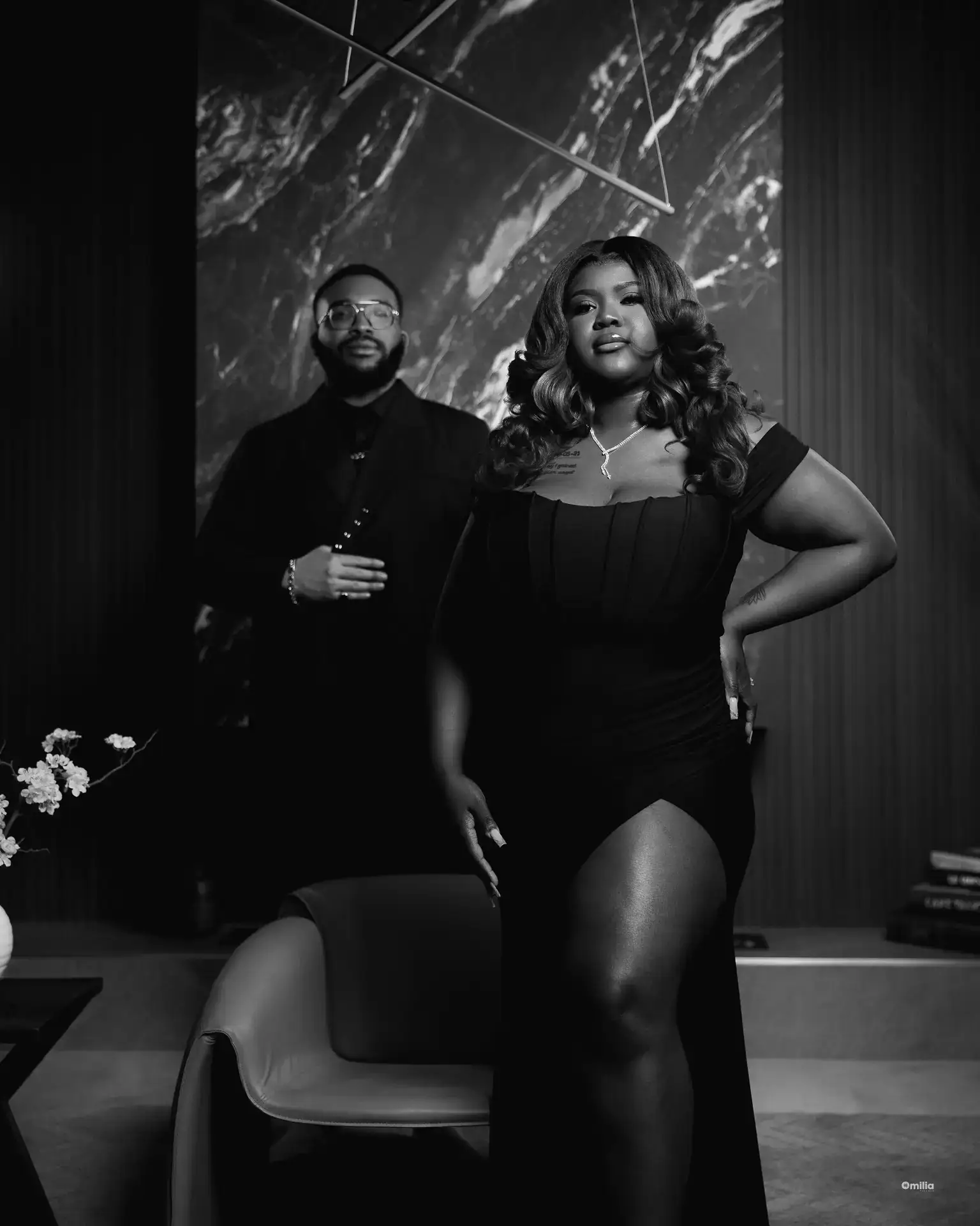 Woman posing hand on hip with partner standing behind in a dark lounge