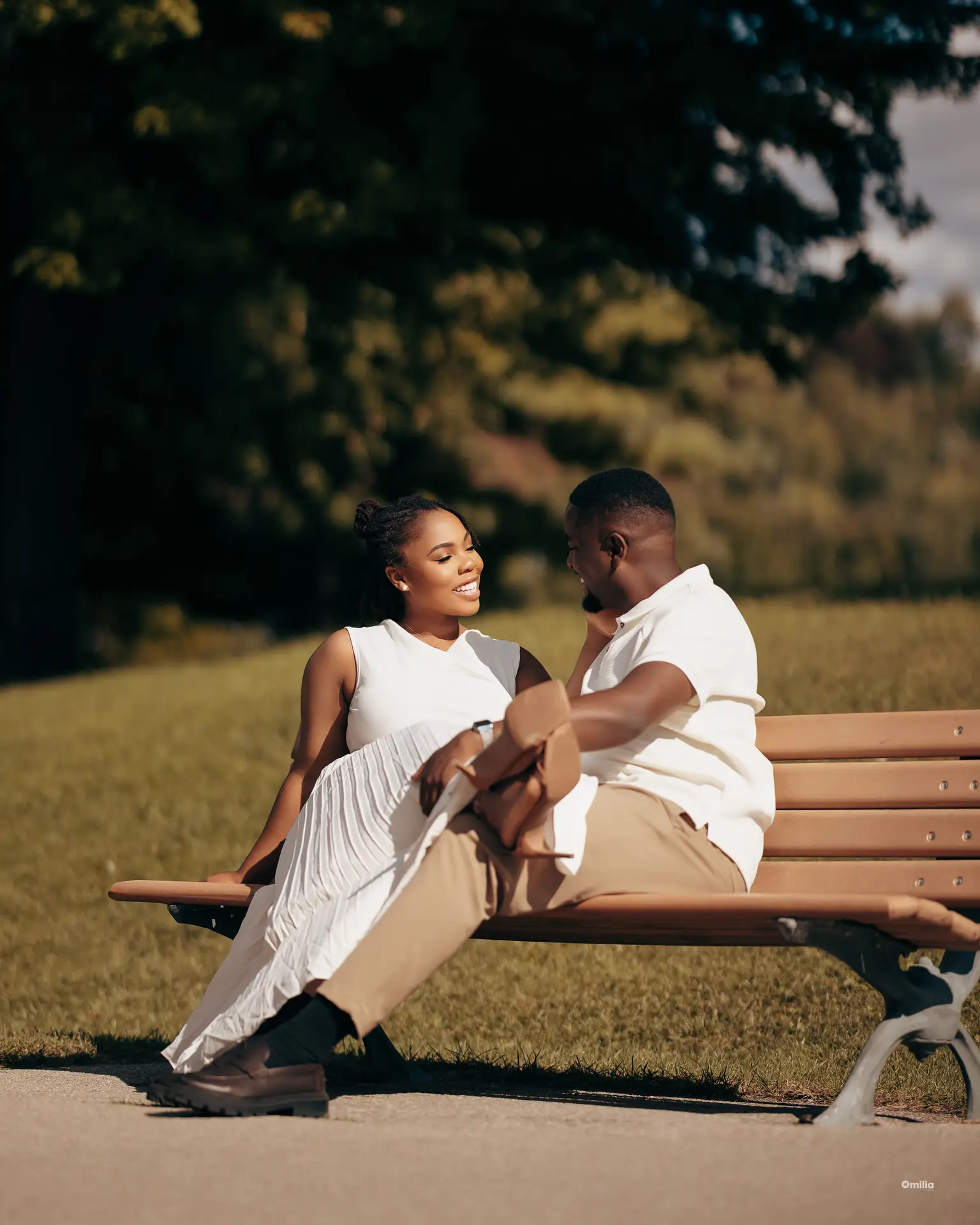 Couple seated on a sunny park bench, her legs draped across his lap