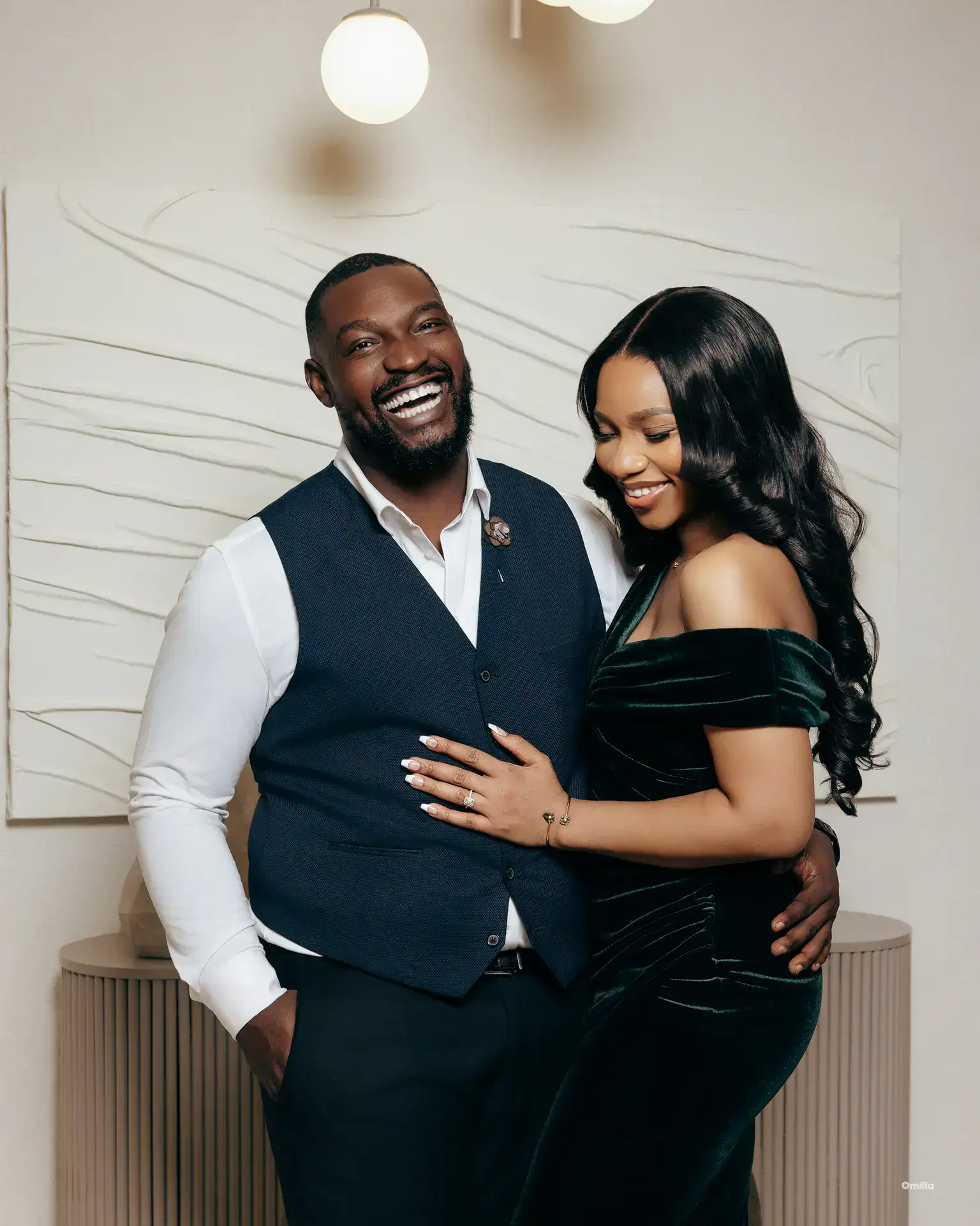Couple laughing in a studio, man in navy vest, woman in green velvet off-shoulder dress