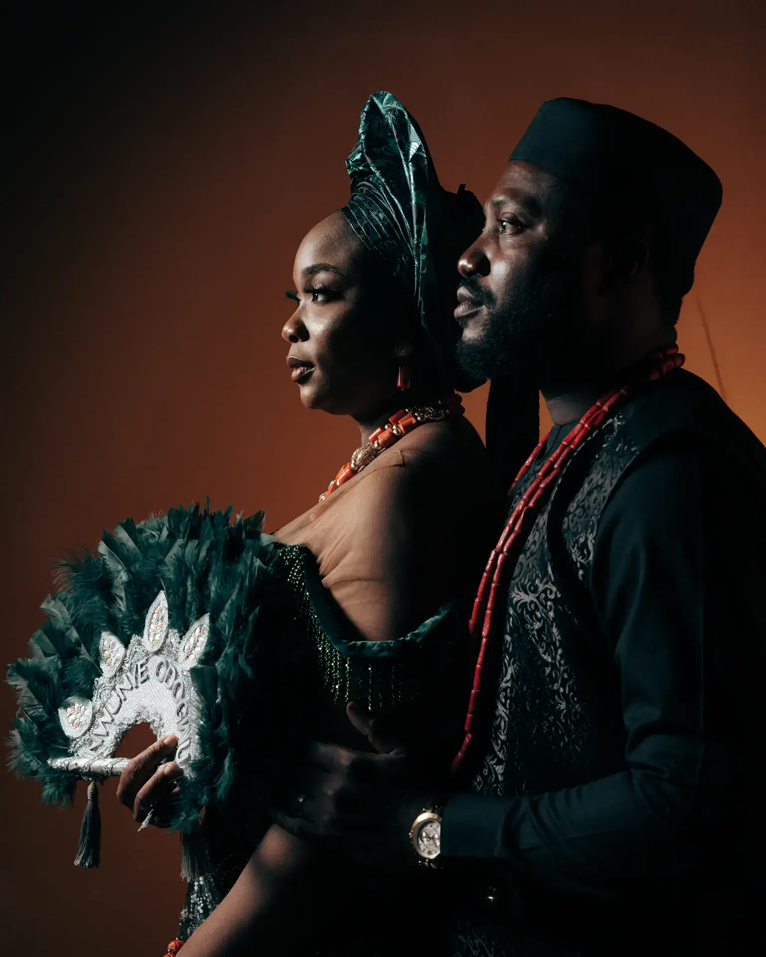 Couple in traditional attire with green gele, coral beads, and feathered fan