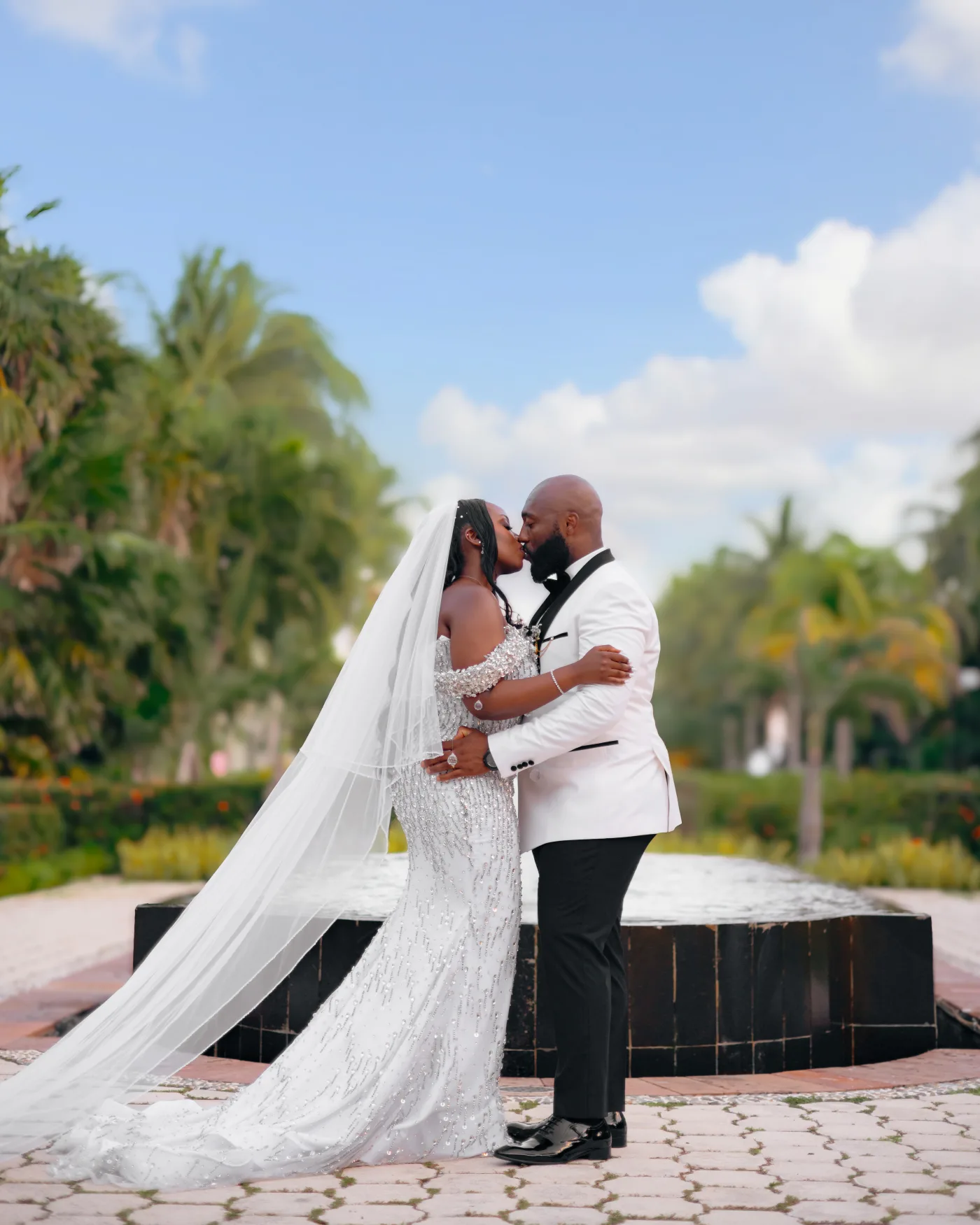 Bride and groom kissing beside a fountain, her veil and train sweeping across the stone