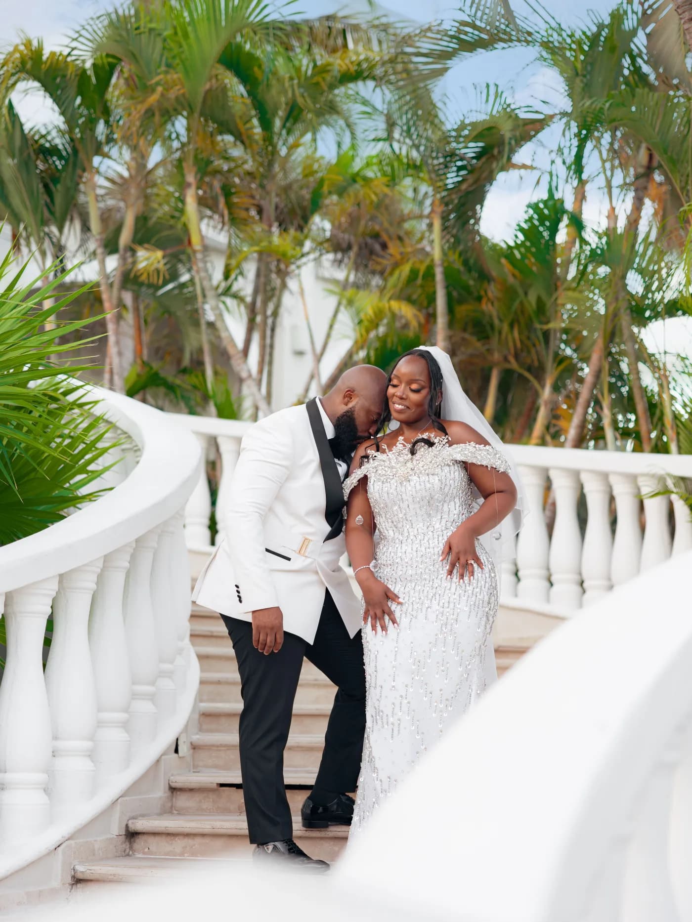 Bride and groom side by side on a curved white staircase framed by palms