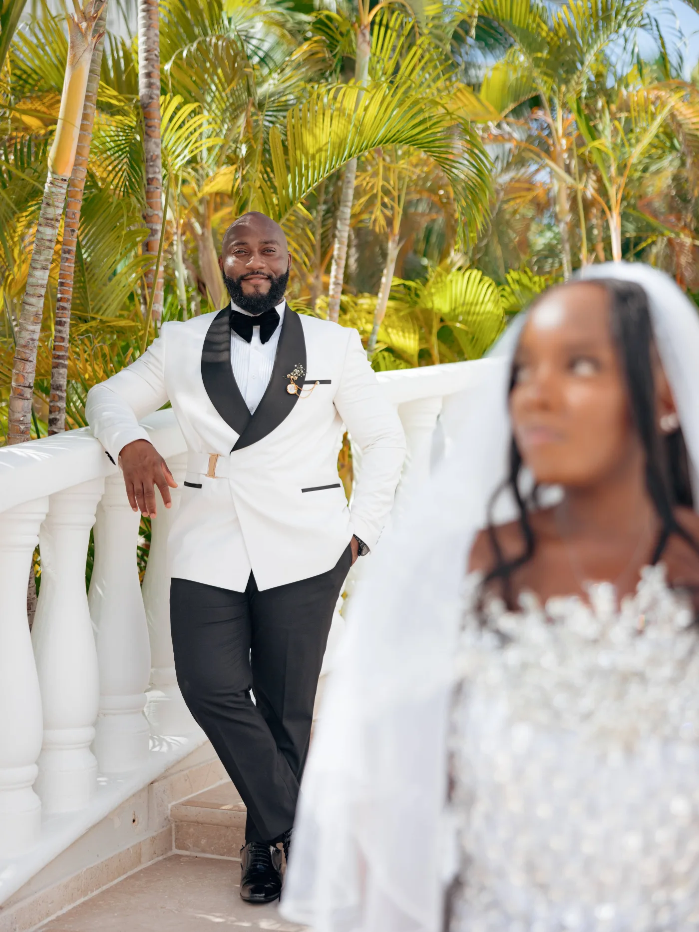 Groom in a white tuxedo as the bride’s veil lifts across the frame in the wind